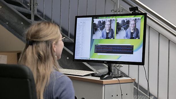 Wissenschaftlerin vor einem Monitor, der im Raum aufgenommene Kamerabilder zeigt